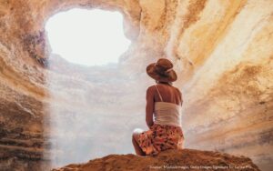 Person sitting in a beautiful cave, with sunlight streaming through an opening to illustrate finding your ikigai.